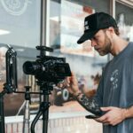 A filmmaker in a casual setting adjusting a professional camera rig for shooting.