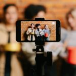 Diverse group of friends filming a video with a smartphone on a tripod indoors.