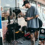 Videographer setting up camera gear outside a shop, capturing a scene.